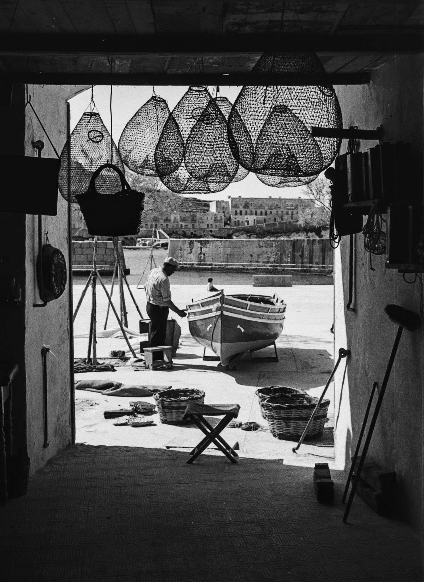 A masterful composition of a fisherman fixing his boat framed within the door frame silhouette, captured by Guido Stilon in 1963. Courtesy of Grace Cilia Vincenti & National Archives of Malta.
