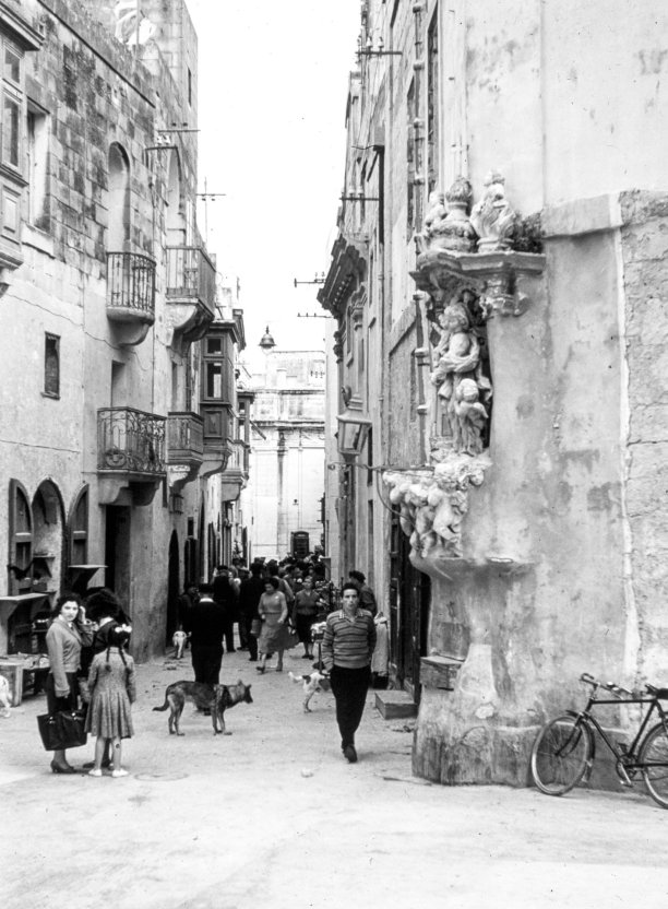A view of the road leading to the Basilica of St George in Victoria, including a corner edifice with a religious shrine, now demolished to enlarge the square; 1964 by Guido Stilon.