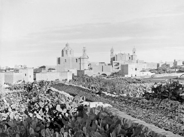 An image showing the old parish church of Nadur being embellished, together with the church of the Sacred Heart of Jesus in the foreground, circa 1914. Attributed to Emanuele Sciortino.