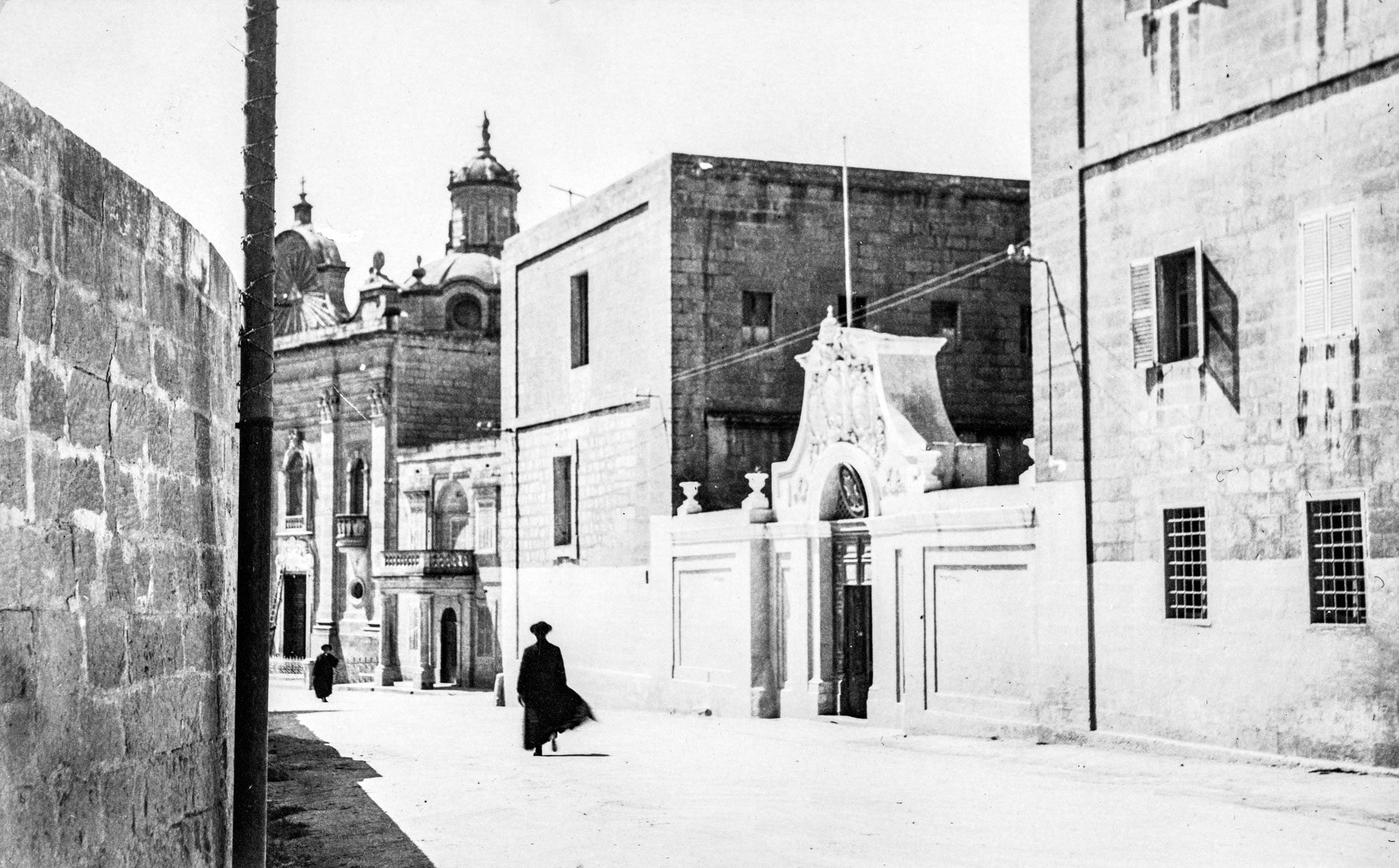 A member of the clergy greets passersby in front of the Seminary in Victoria, Gozo, circa 1950; photographer unknown.